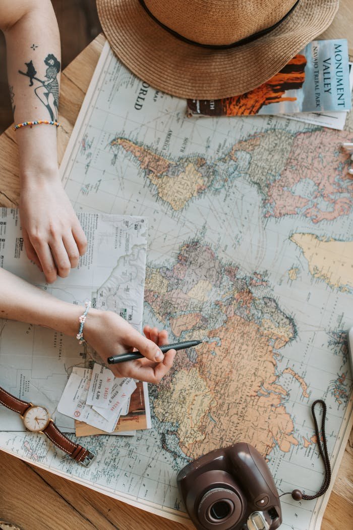 Person planning a journey with a world map, camera, and travel guide on a wooden table.