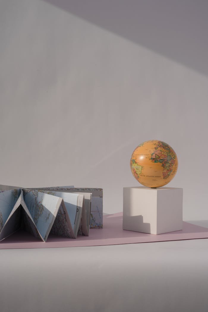 Artistic still life featuring a globe and folded maps on a pastel backdrop.